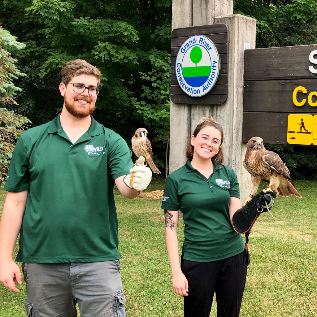two university students stand with birds of prey perched on their hands