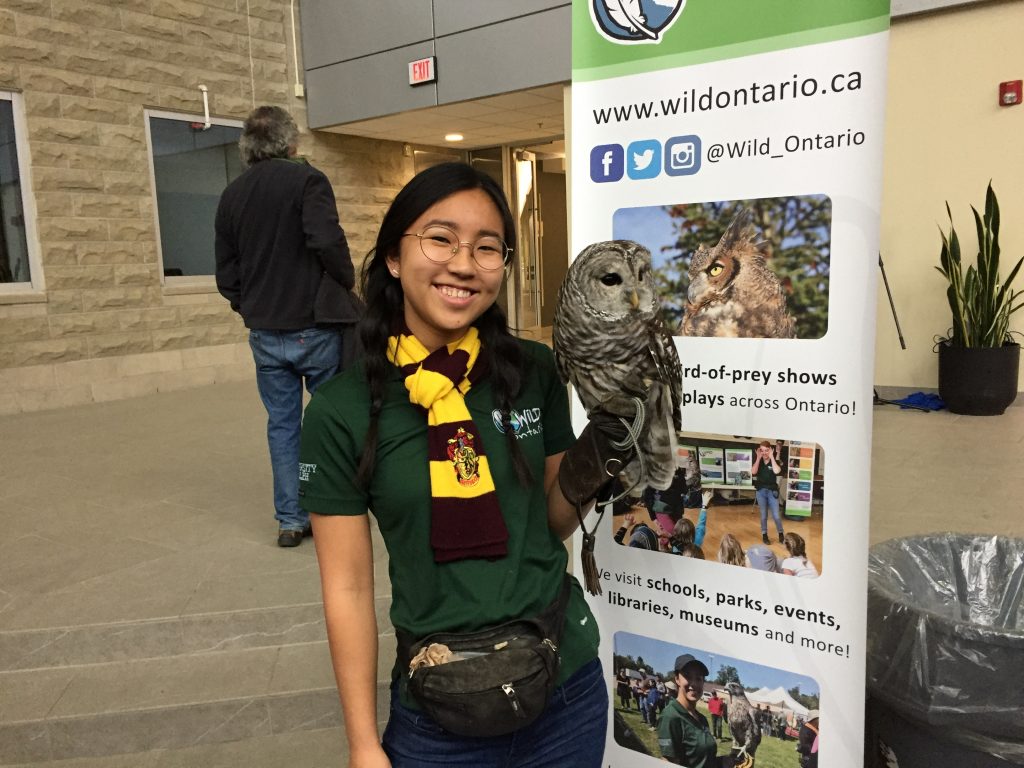 a handler with an owl stands in front of an educational sign