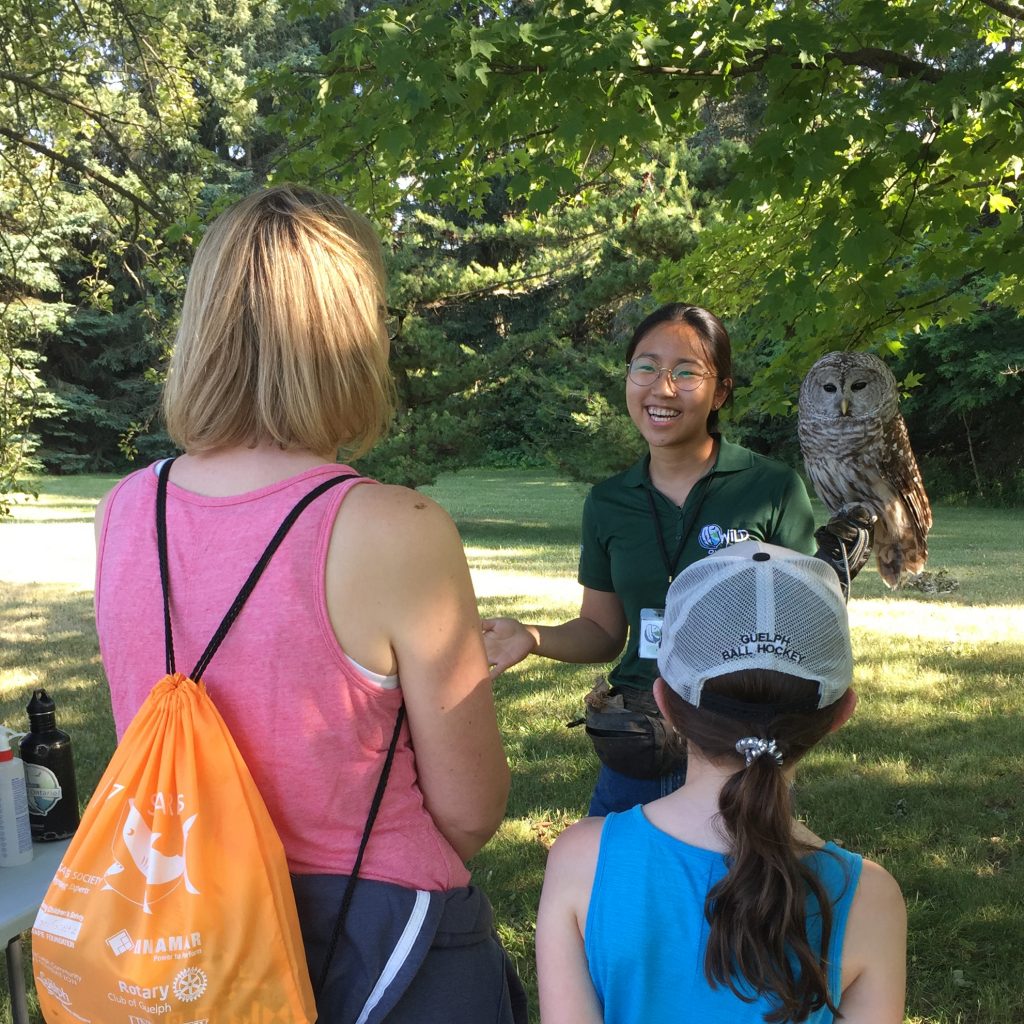a university student is handling an owl and speaking to a mother and daughter